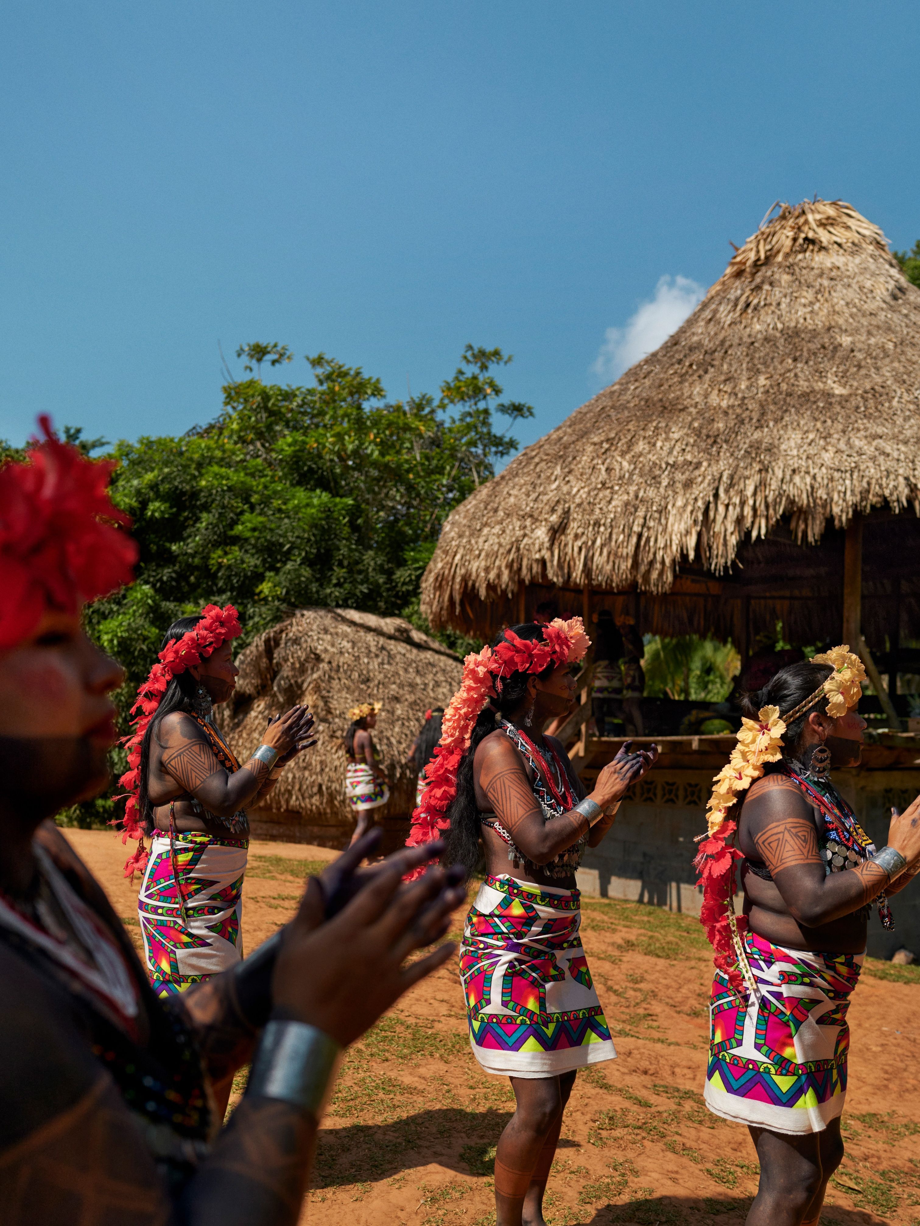 Tribe members in the Emberá village of Parara Purú wearing floral headdresses and brightly colored fabric skirts clap their hands