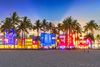 Colorful lights illuminate the buildings on Ocean Drive at night in Miami with palm trees and the beach in the front.
