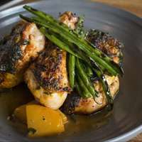 A plate of roast chicken topped with charred green beans is served on a blue ceramic plate at restaurant Virtue in Chicago, Illinois