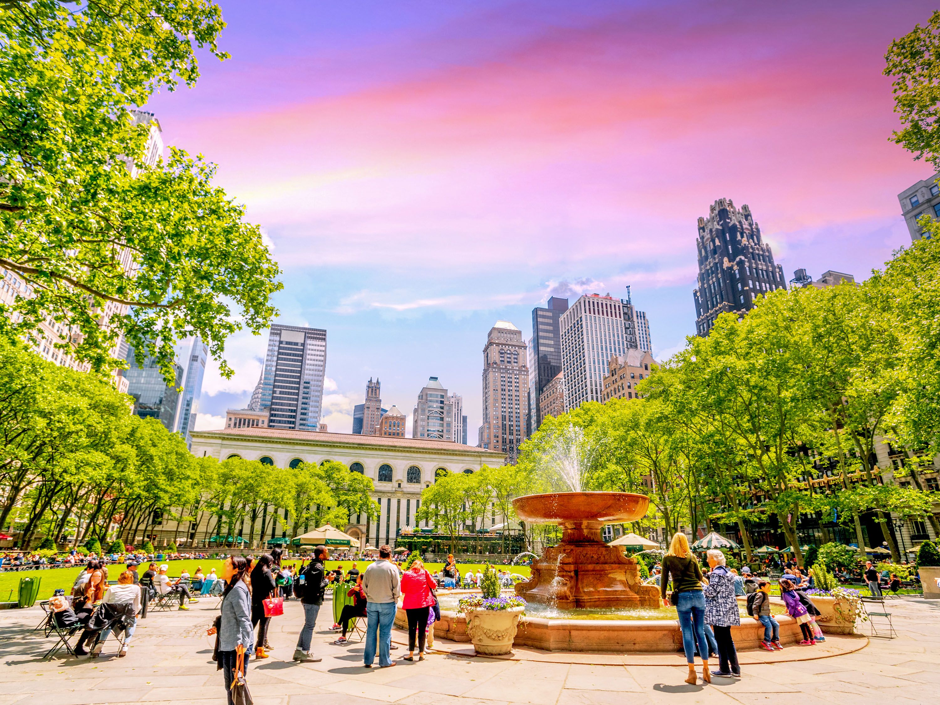 People gathered around a fountain in an urban park with skyscrapers in distance.
