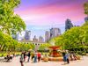 People gathered around a fountain in an urban park with skyscrapers in distance.