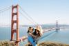 A smiling woman holds a girl with San Francisco's Golden Gate Bridge in the background