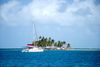 A sailboat cruises in bright blue waters near an island filled with small buildings and palm trees.