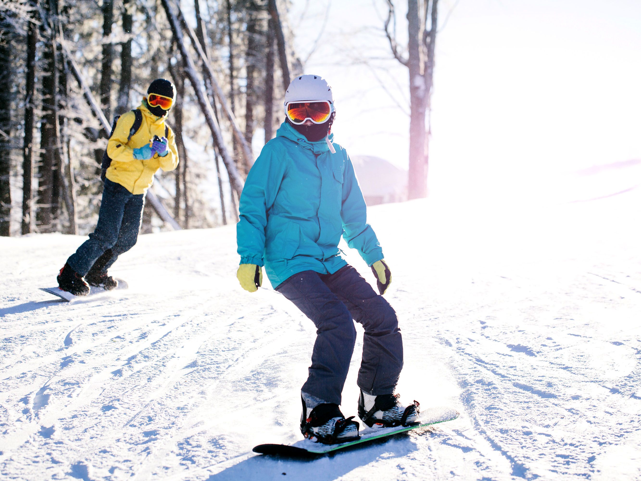 Snowboarders in yellow and blue jackets travel down a mountain in the snow.