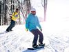 Snowboarders in yellow and blue jackets travel down a mountain in the snow.