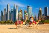 Two camels withone rider pass by on Jumeirah beach with skyscrapers in the background in Dubai.