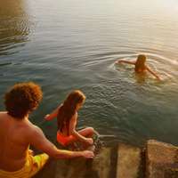 Three kids wade into the sea from stone steps