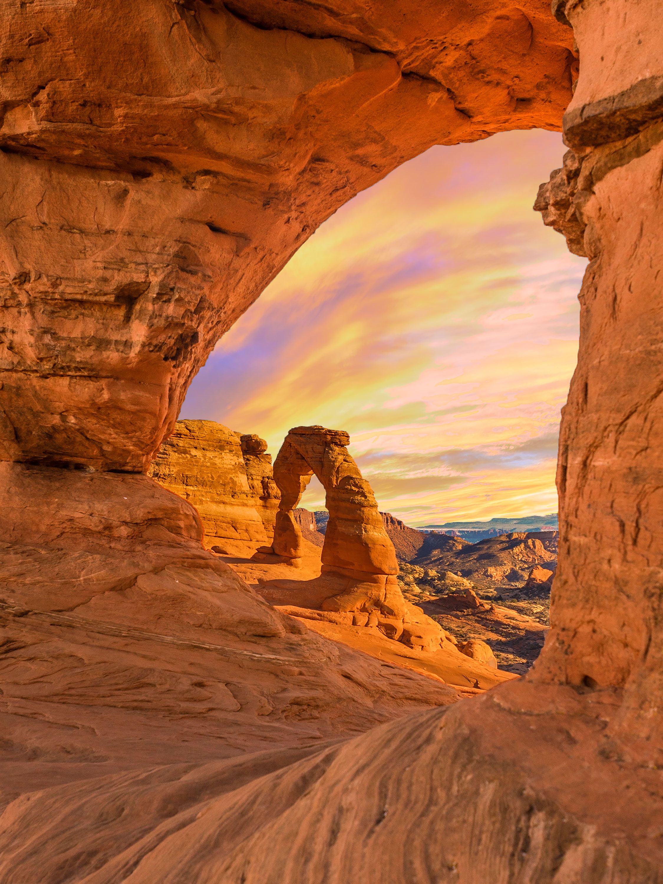 A delicate Arch framed by sandstone window at colorful sunset.