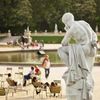 A classical sculpture of a man in Jardin de Luxembourg, Paris, with an ornamental lake seen behind and tourists seated and walking