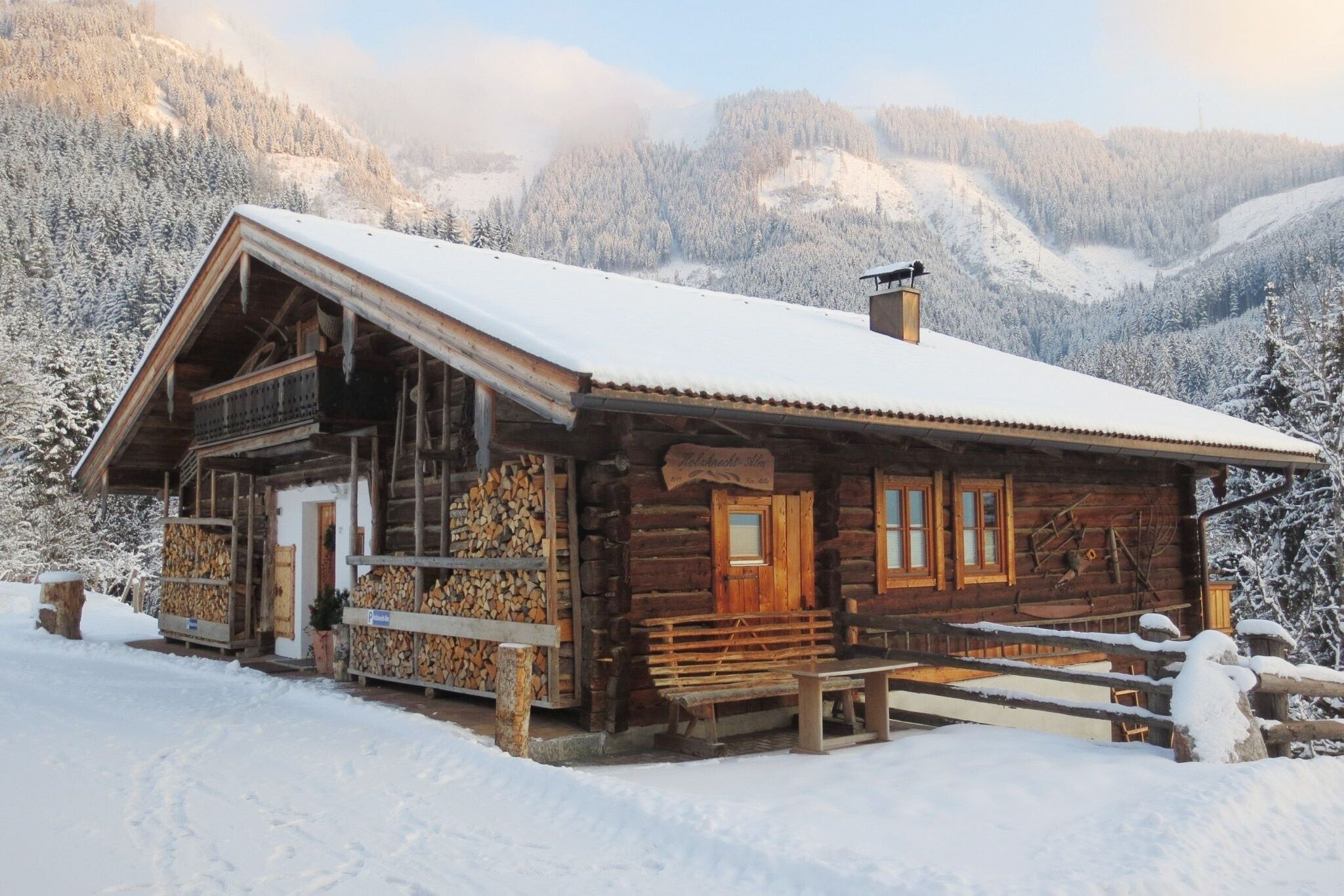Eine eingeschneite Berghütte aus Holz, im Hintergrund eine Berglandschaft 