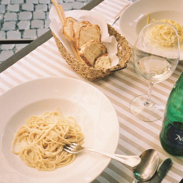 Two bowls of spaghetti, a basket of bread and a glass of wine sit atop a table covered with a pink and white striped tablecloth in Italy