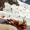 A board of appetizers and a glass of wine is served at an après-ski resort in the French Alps while people ski down the mountain below