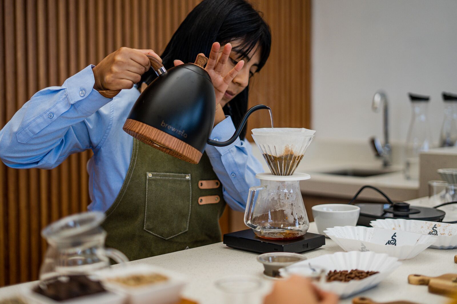 A barista in an apron pours water from a kettle into a filter over a coffee pot at Sisu Coffee Studio in Panama City