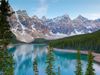 Large snowcapped mountains are seen before a vibrant blue lake with tall green trees in the foreground