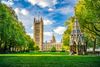 Victorian gothic monument on grassy lawn with tall tower and historic building behind.