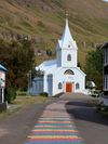 A painted rainbow path leading to a blue church in Seydisfjördur, Iceland