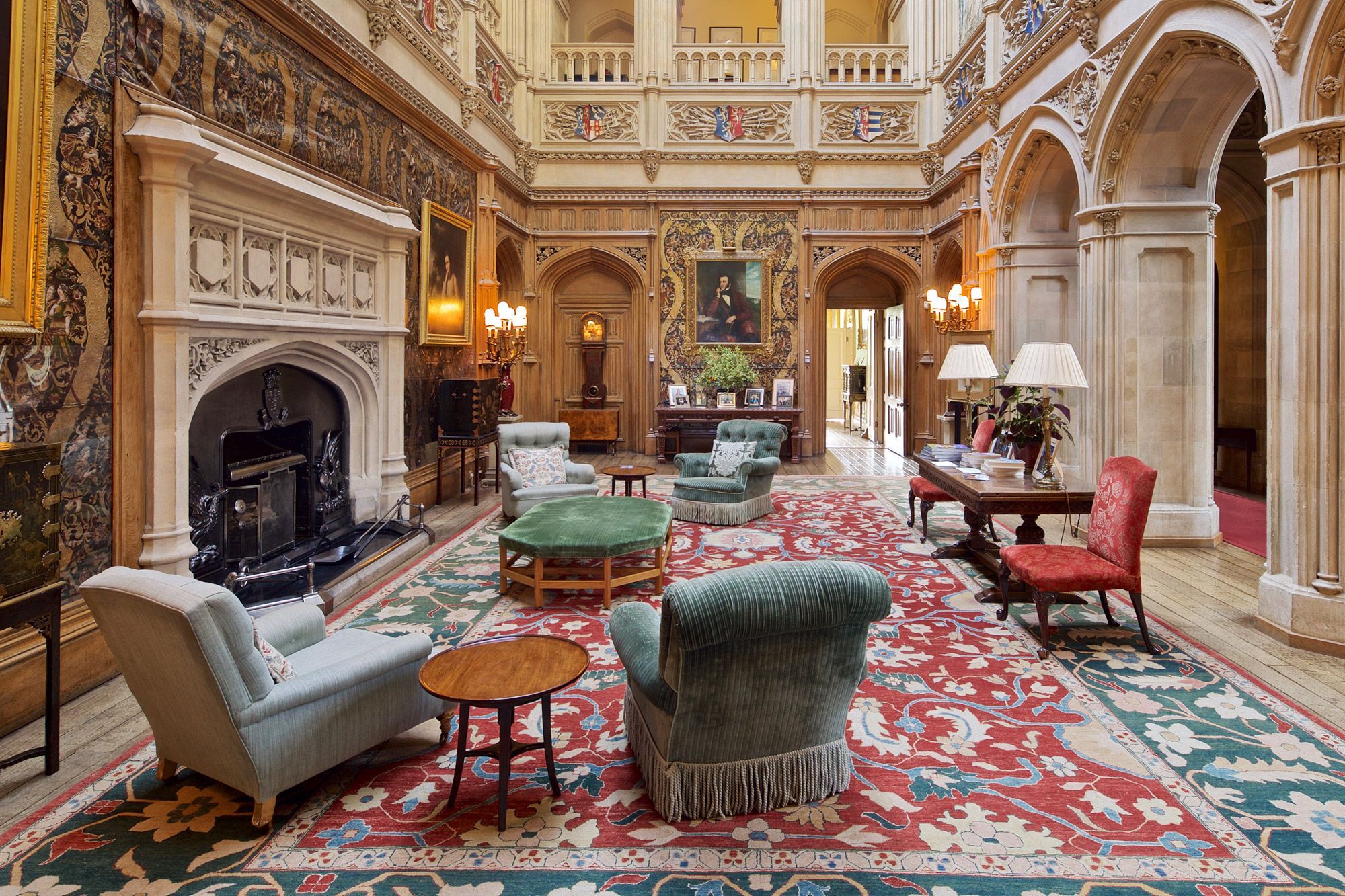 Ornate wall decorations and pillars with green arm chairs and a rug in the interior space of Highclere Castle.