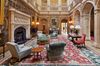 Ornate wall decorations and pillars with green arm chairs and a rug in the interior space of Highclere Castle.