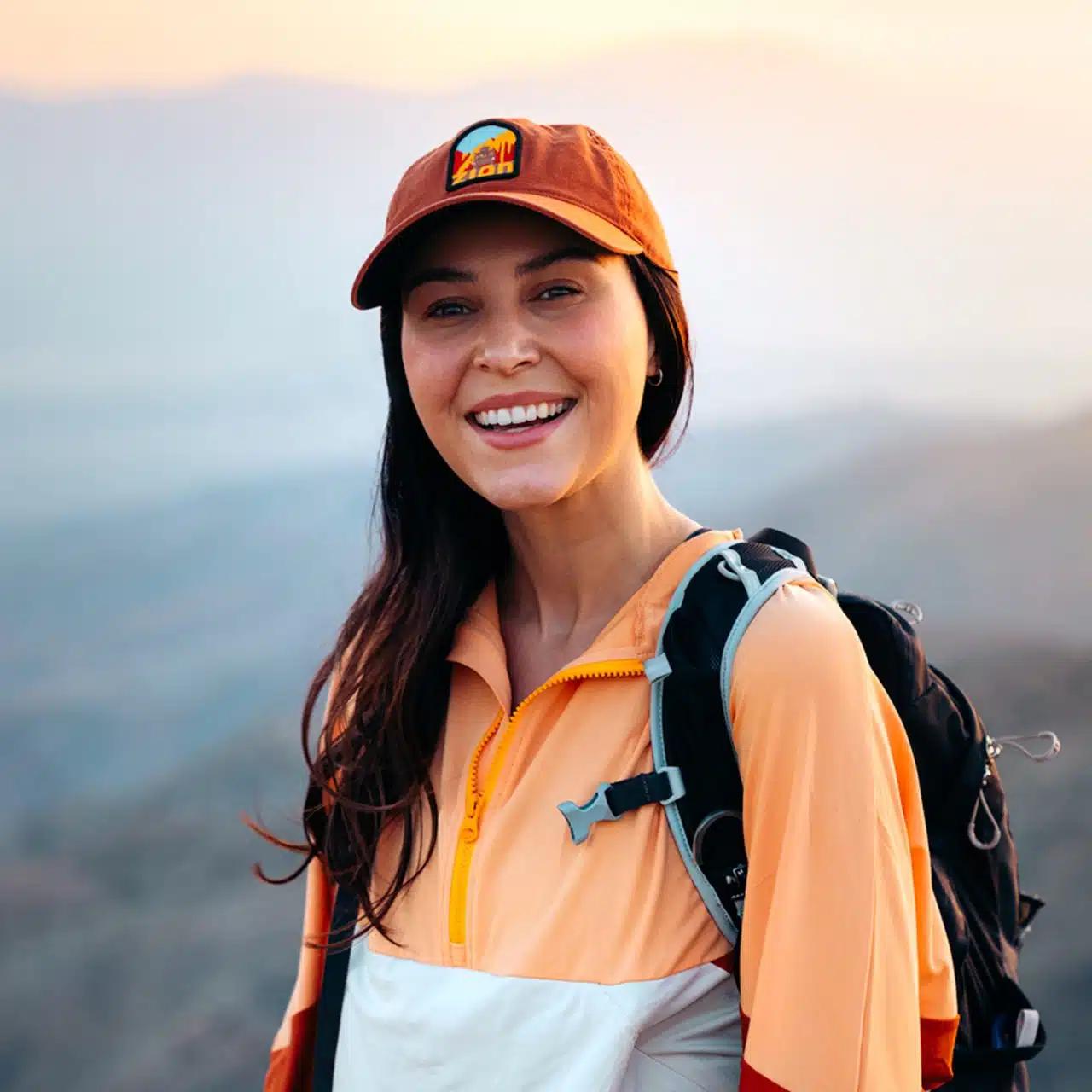 Travel influencer Renee Hanel, aka Renee Roaming, wears an orange cap and windproof jacket and smiles for a photo in Joshua Tree, California