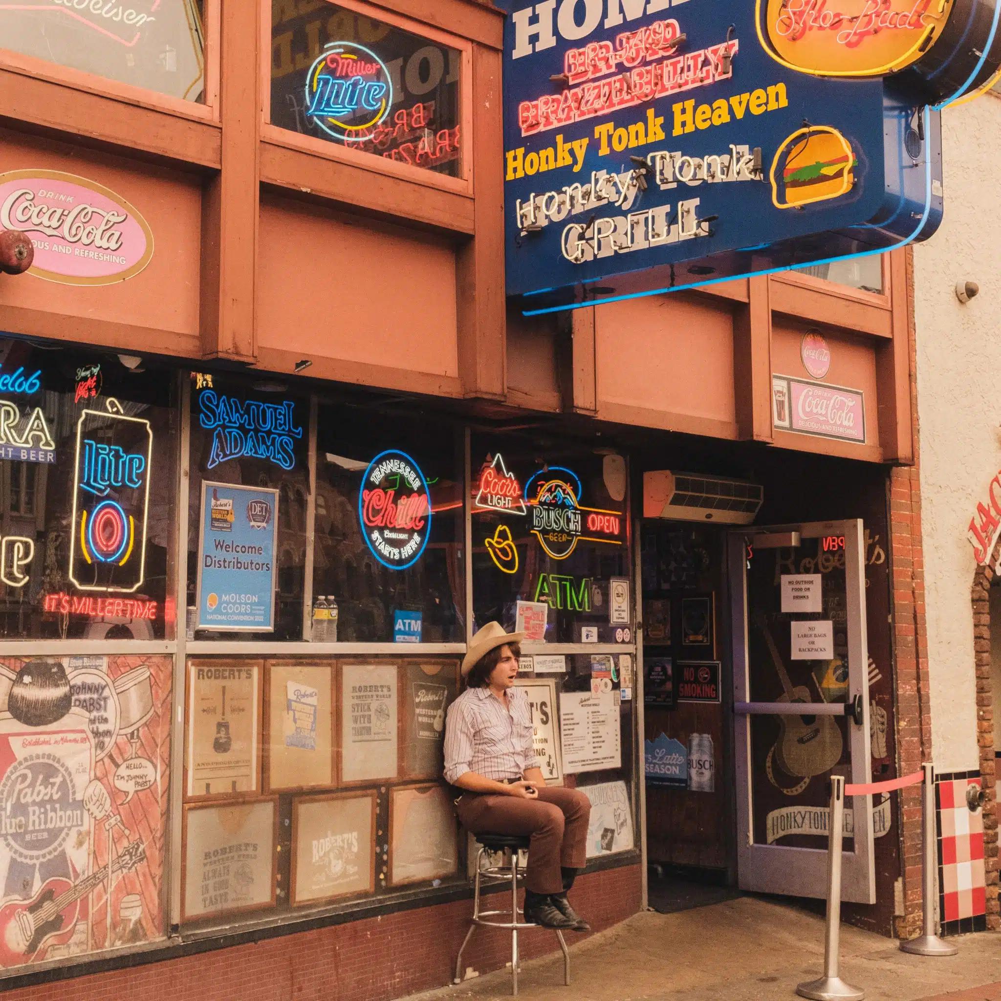 A person wearing a cowboy hat sits out front of a honky-tonk bar in Nashville, Tennessee