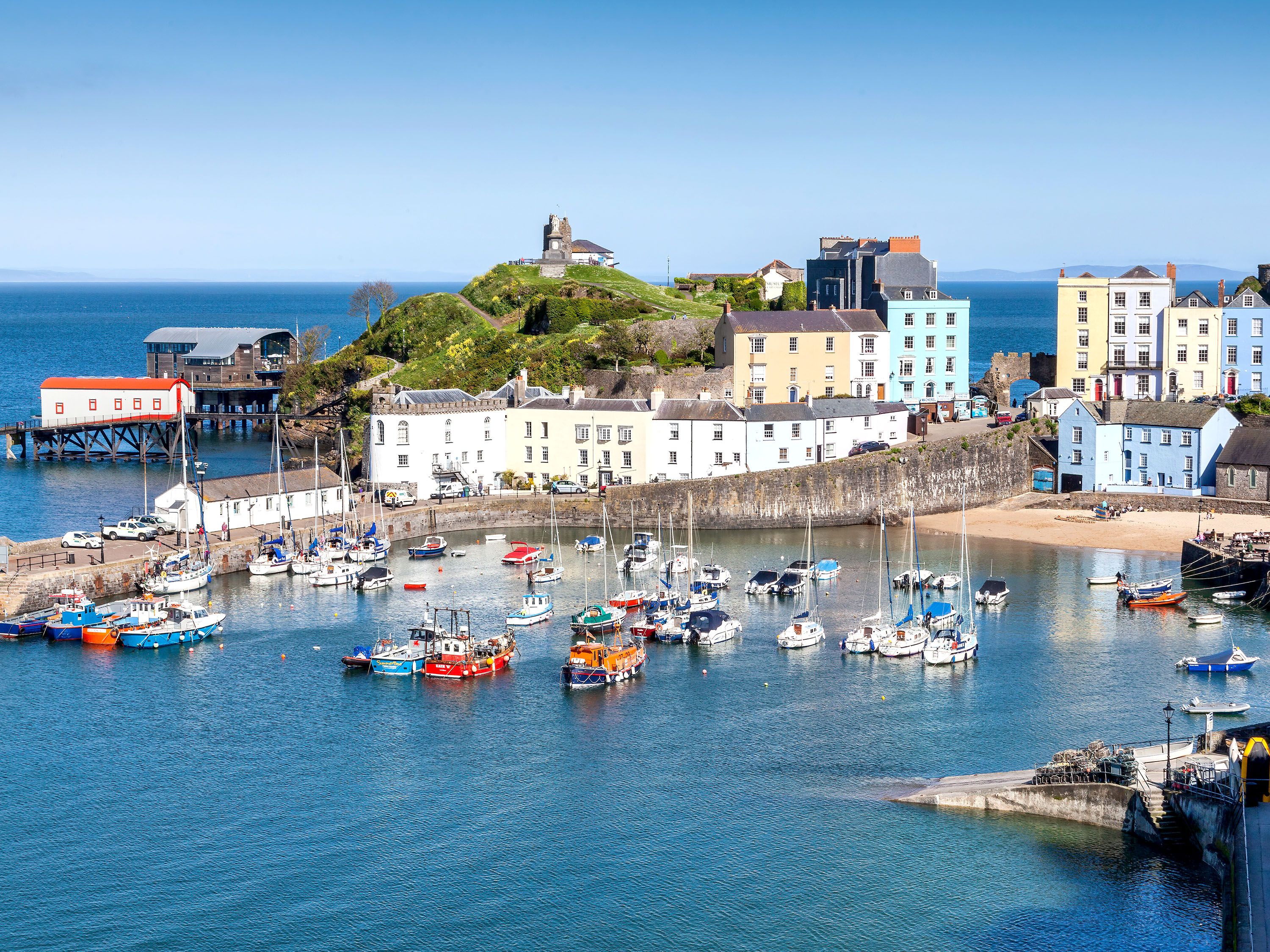 Harbor with sailboats and fishing boats on moorings with colorful buildings on shore.