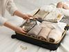 Woman’s hands placing neatly organized travel items into a small suitcase on a bed.