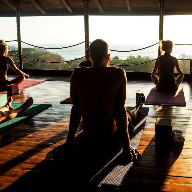 An open air yoga class on a wooden floor, overlooking a view of the sea
