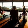An open air yoga class on a wooden floor, overlooking a view of the sea