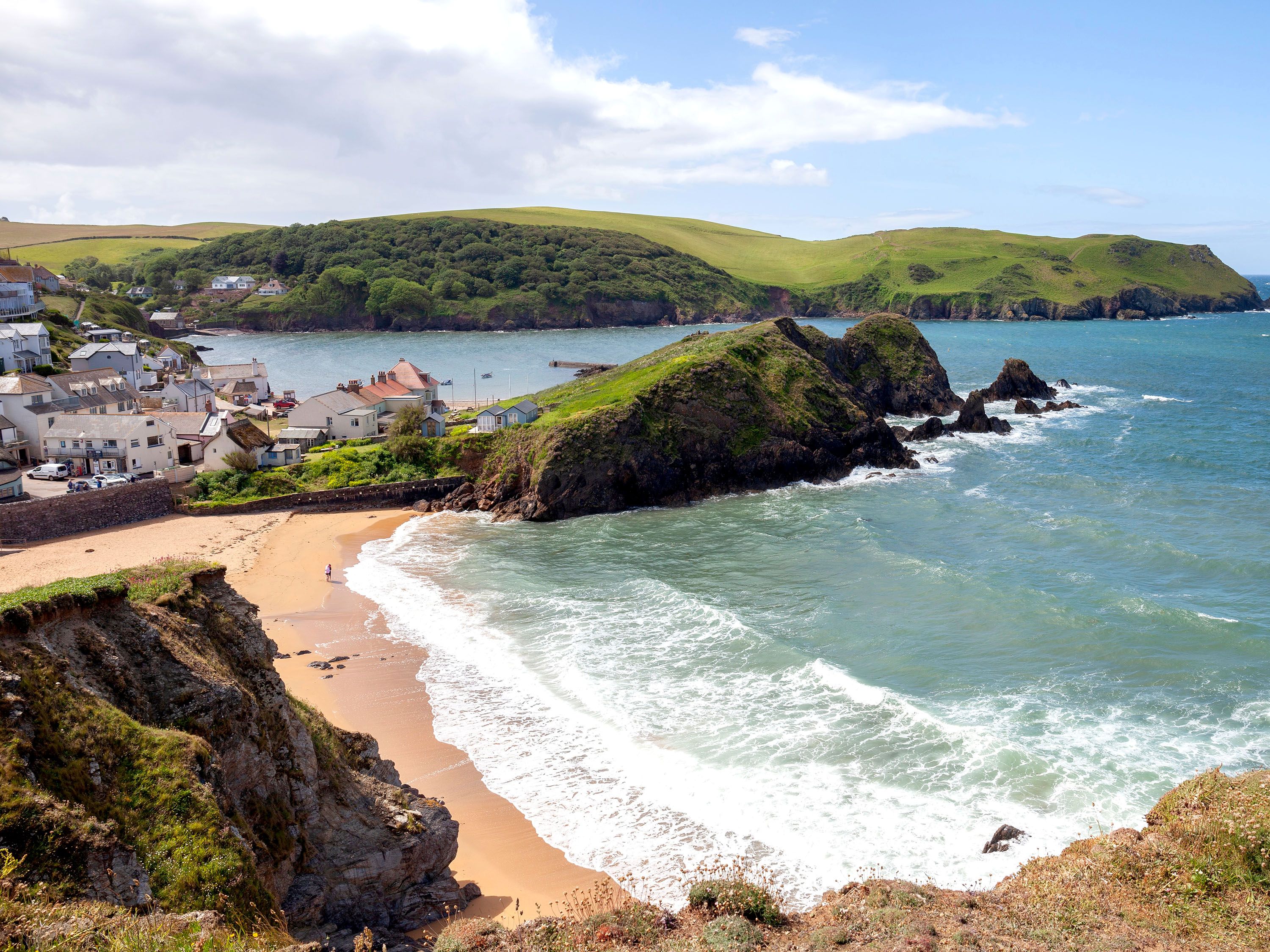 Overhead view of beach and surf area with small cottages and green bluffs.