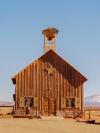 A small wooden church with a belltower stands on an empty plain, with a mountain range in the far distance behind it