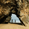 Walkers visible through an arch in a huge rock on the sand Praia da Adraga, Portugal