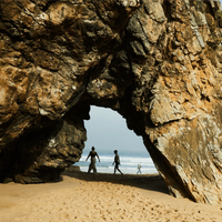 Walkers visible through an arch in a huge rock on the sand Praia da Adraga, Portugal