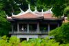 People stand inside a red-roofed Chinese-style pavilion surrounded by lush greenery in Shinjuku Gyoen National Garden, Tokyo.