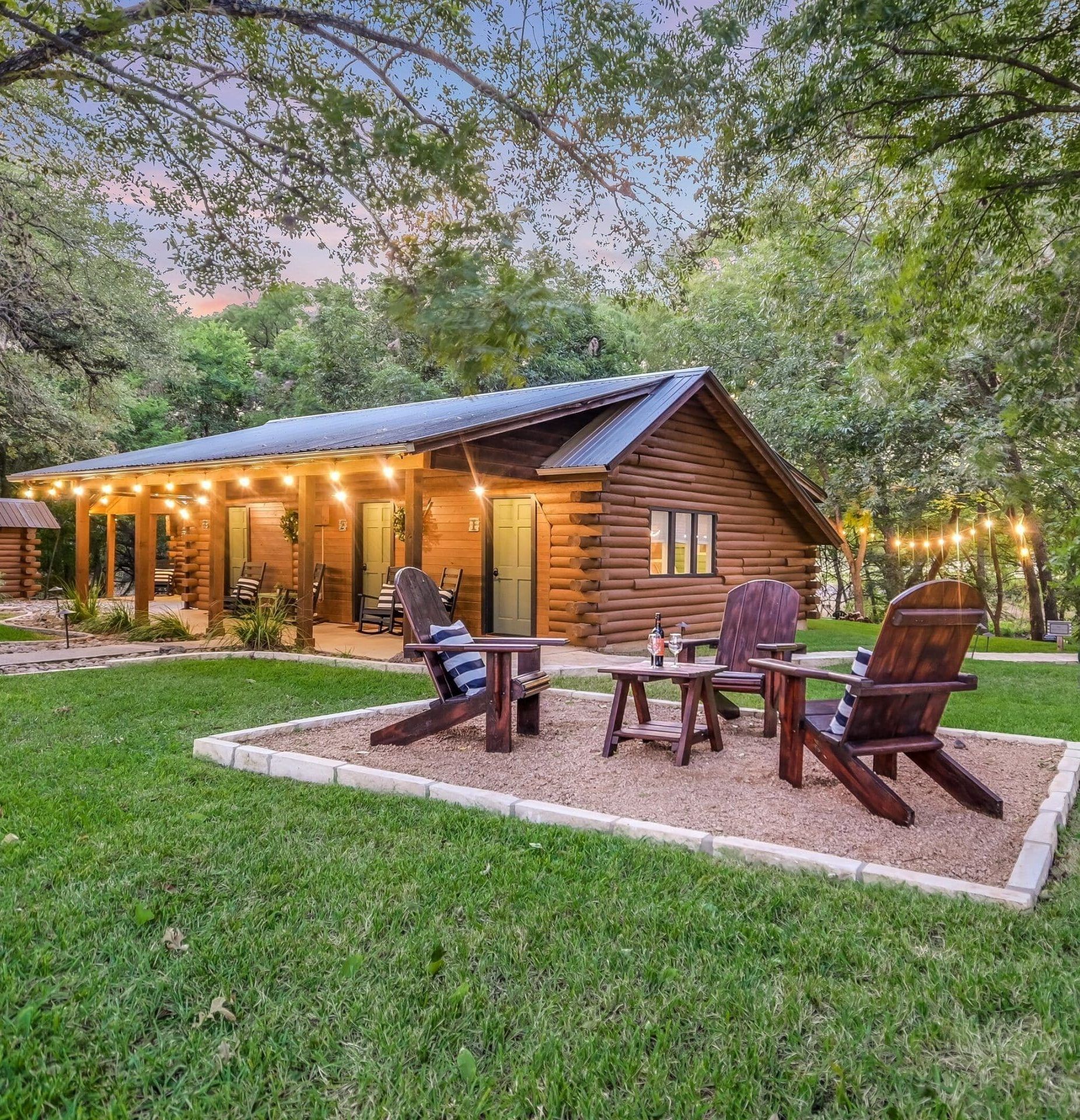 A log cabin Vrbo with adirondacks in the yard, in Wimberley, Texas