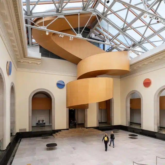A large orange staircase, designed by Frank Gehry, at the bottom of an exhibition space at the Art Gallery of Ontario, Toronto