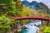 The iconic red Shinkyo Bridge arching over a green-toned river in Nikko, Japan, with trees lining both riverbanks.
