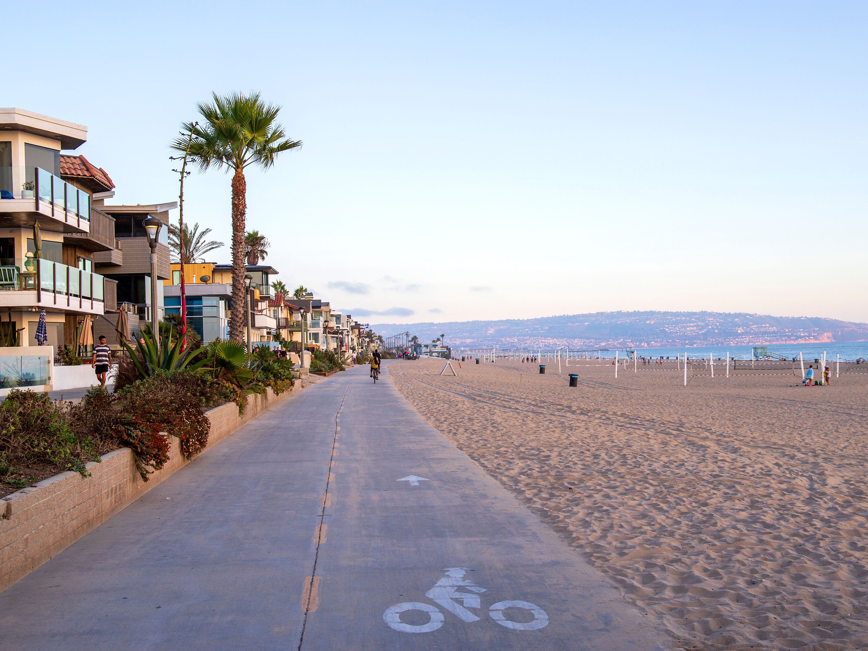 Bicycle path with sandy beach, palm tree and buildings.