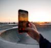 A person holds up a smartphone to take a photo of a sunset at Venice Beach Skate Park in California