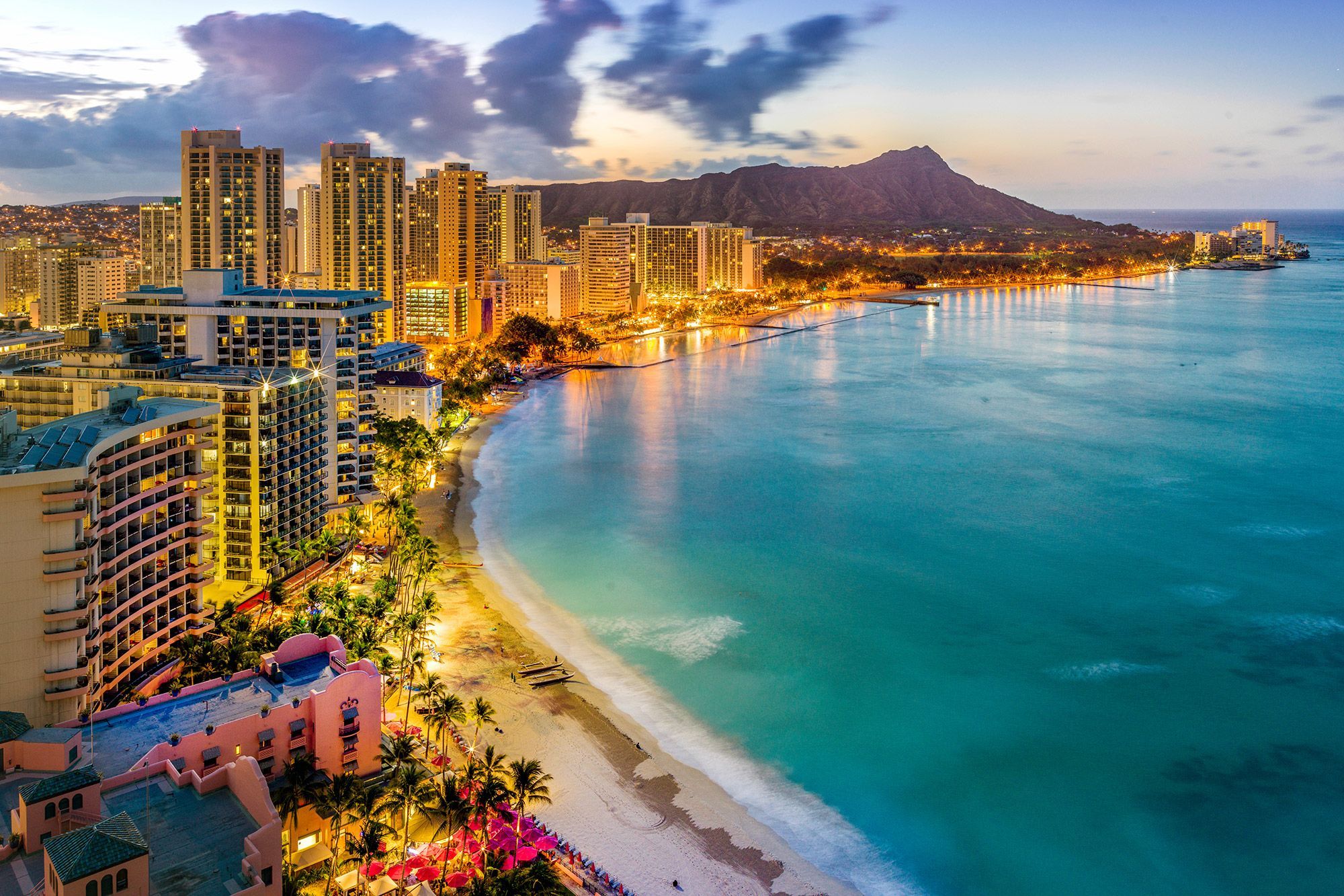 Aerial view of buildings lit up during sunset along Waikiki Beach in Honolulu.