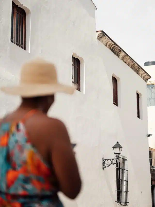 A woman in a straw hat walks past a whitewashed colonial building in Santo Domingo; visit in December through April for the best weather