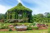An Ivy-covered garden pavilion surrounded by blooming roses and manicured greenery.
