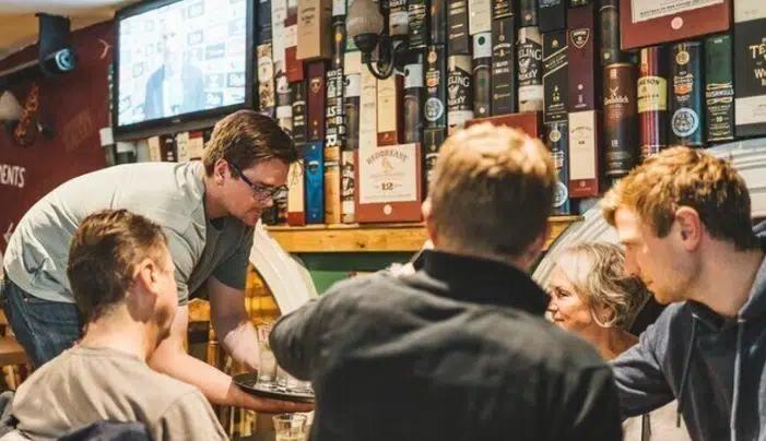A man sets a tray of drinks down for four drinkers at the table in a traditional Dublin pub