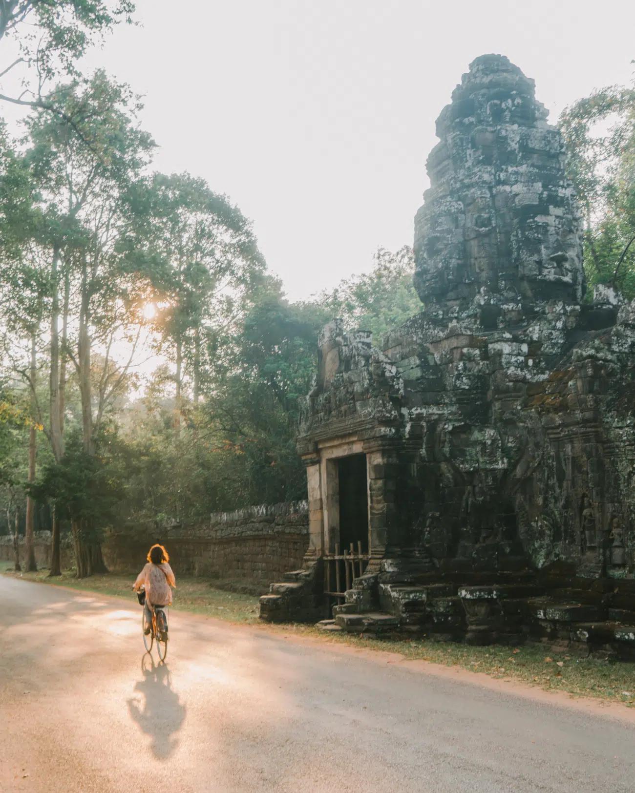 A female cyclist rides past the entrance to an ancient stone temple