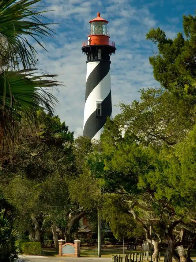 The black-and-white striped St. Augustine Lighthouse & Maritime Museum is framed by trees with a blue sky behind