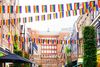 A city street decorated with rows of rainbow pride flags hanging across the roadway and along building façades, creating a vibrant, festive atmosphere.