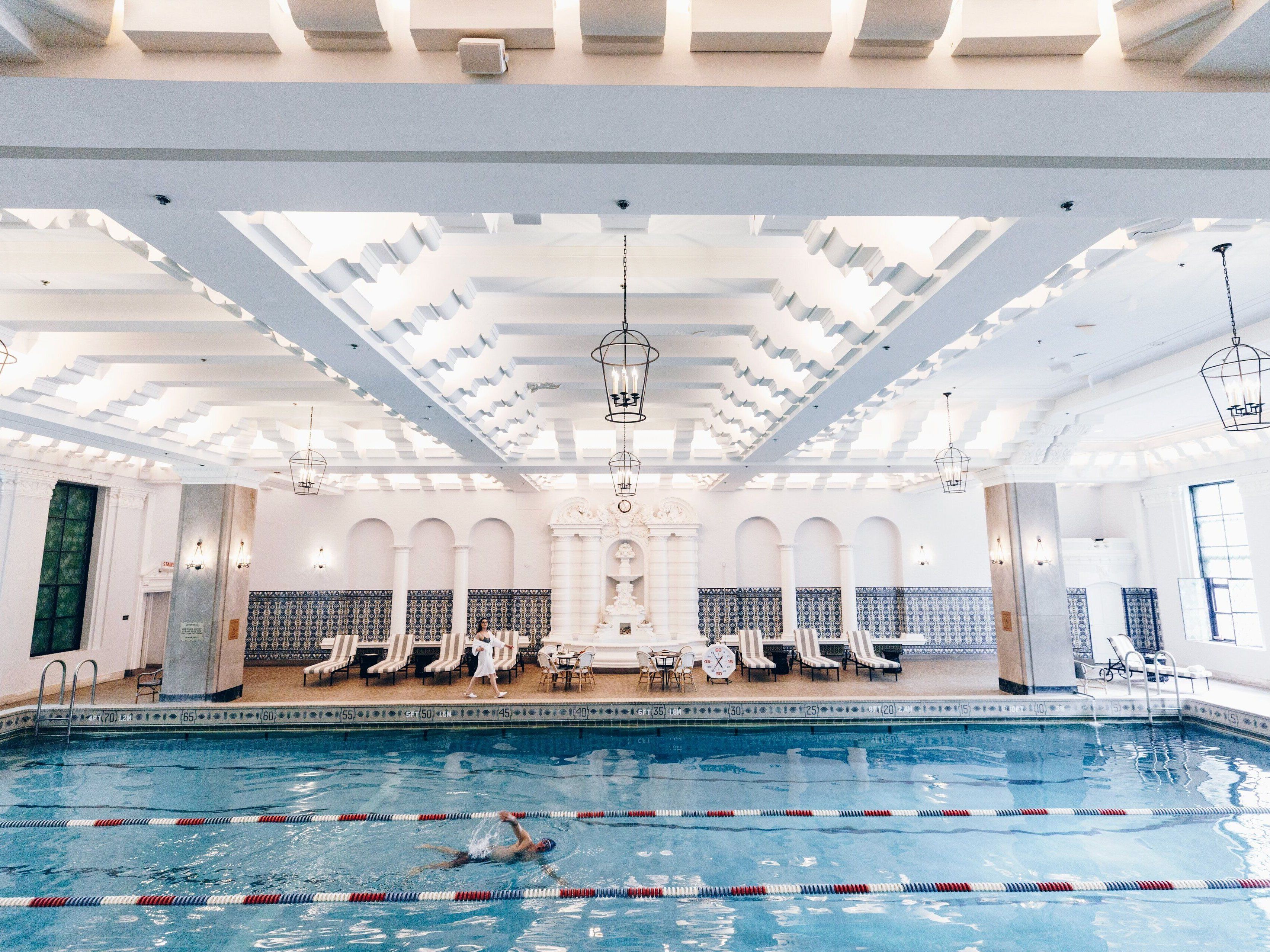 A man swims in a large lap swimming pool in a hotel with bright natural light.