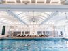 A man swims in a large lap swimming pool in a hotel with bright natural light.