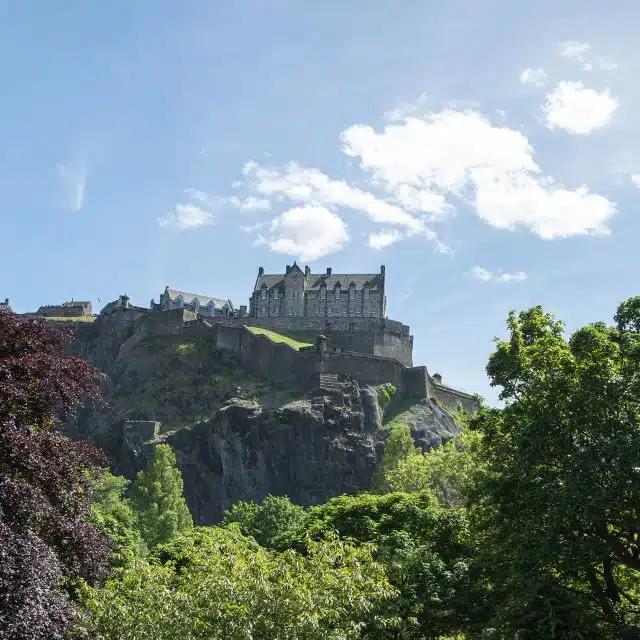 Edinburgh Castle as seen from below, with trees in the foreground and a bright blue sky beyond