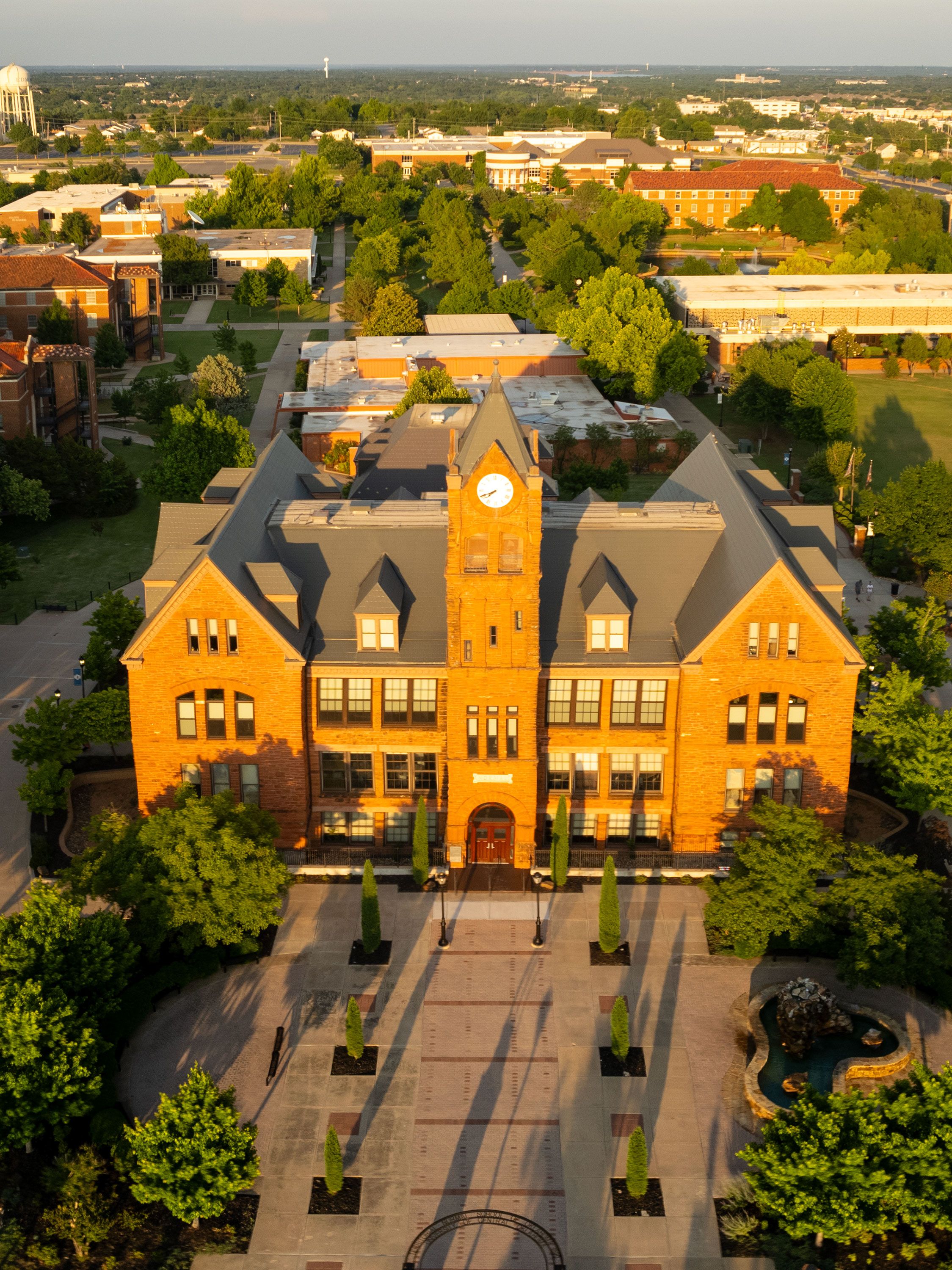 An aerial view of red-brick campus building with central clock tower and tree-lined walkways.