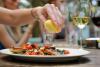 A woman's hand squeezes lemon over a plate of pan-fried fish, with a glass of white wine alongside
